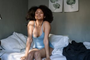 Woman with curly hair enjoying a peaceful morning in her cozy bedroom with sunlight streaming in.